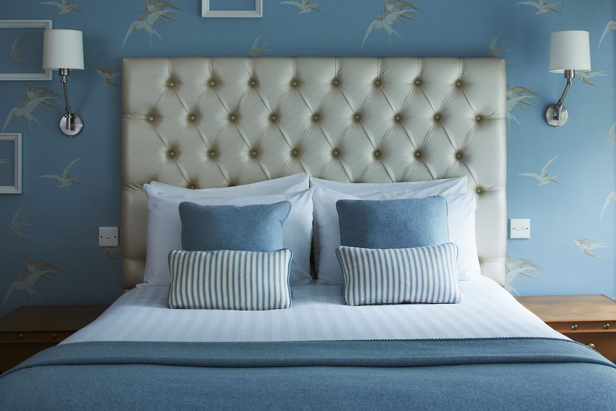 A bedroom with a tufted headboard, two pillows, a bedspread, and wall-mounted lamps.