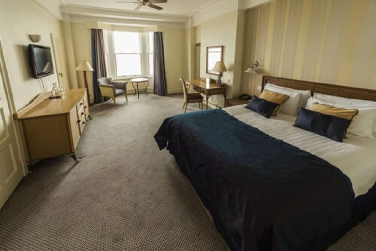 A hotel room with a large bed, a desk, a chair, and a television on the wall.