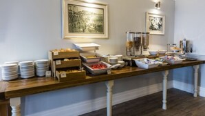 A buffet setup with plates, bowls, and food containers on a wooden table. - The Old Ship Hotel (Brighton)