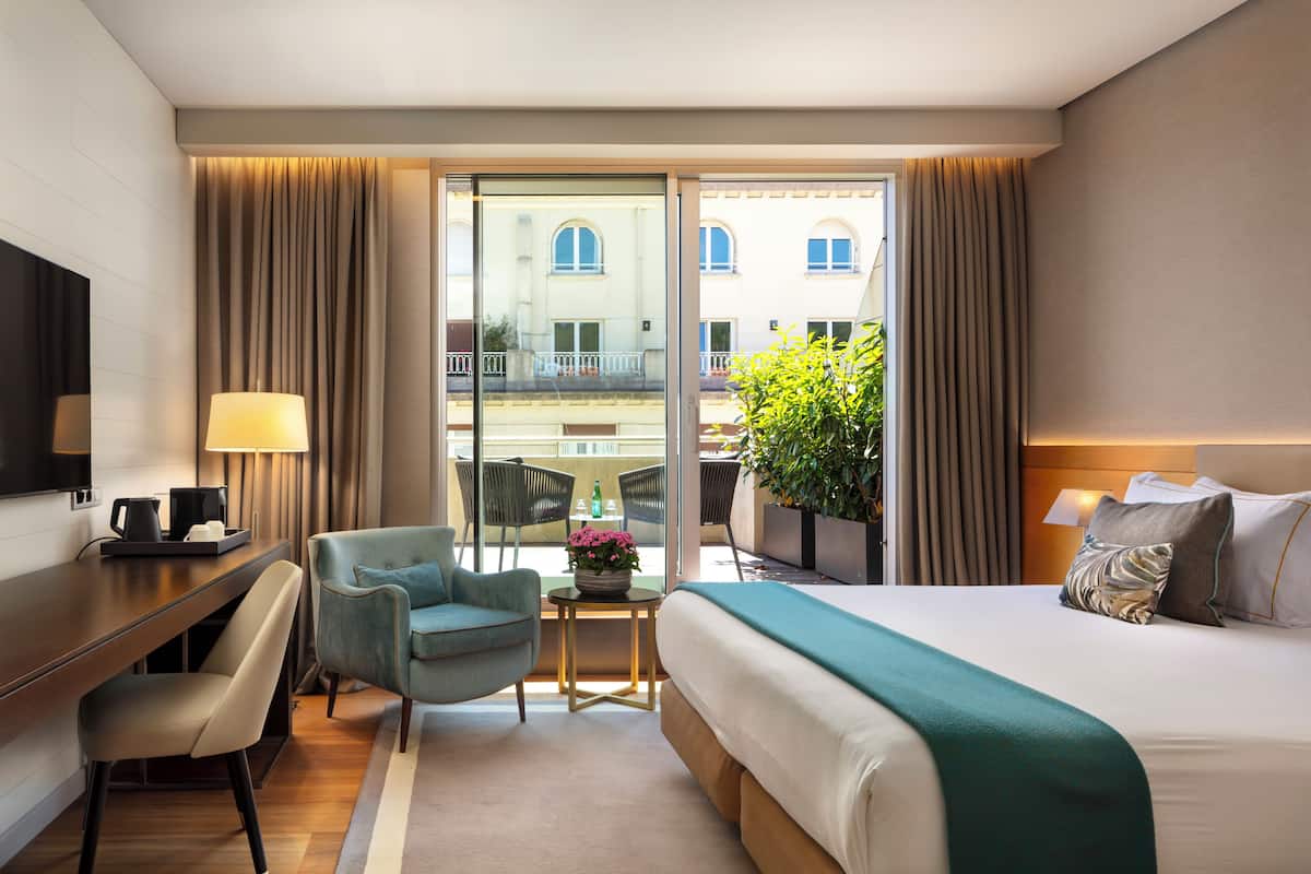 Habitación de hotel con cama, escritorio, silla y vistas al exterior.