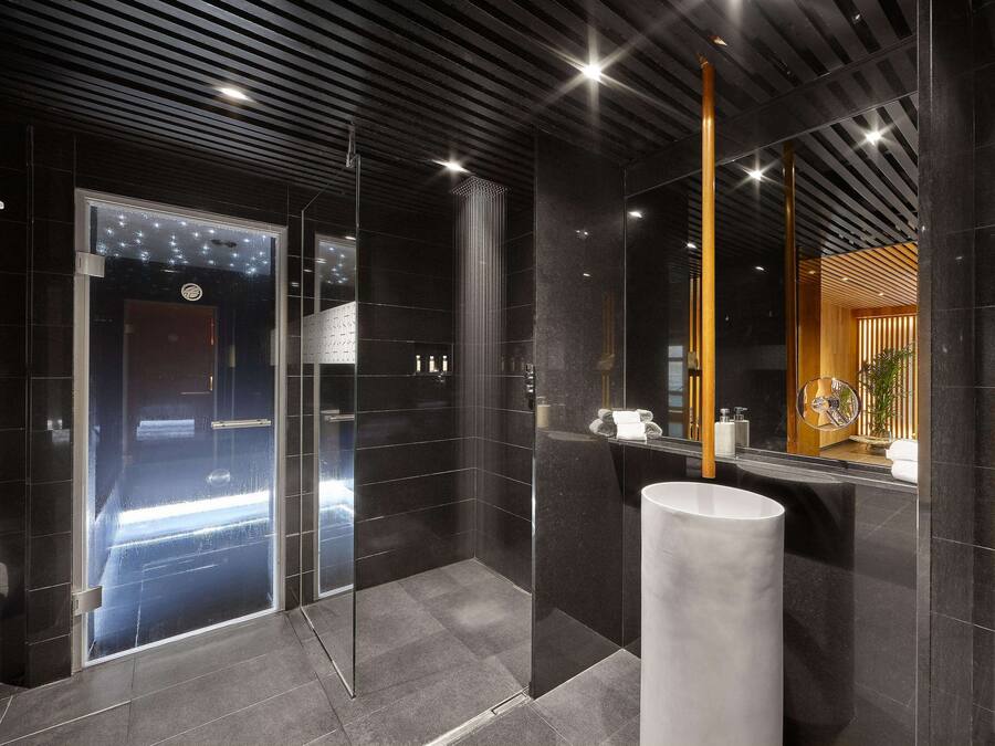 Un baño moderno con cabina de ducha de vidrio, un lavamanos grande de color blanco y un espejo con marco de madera.