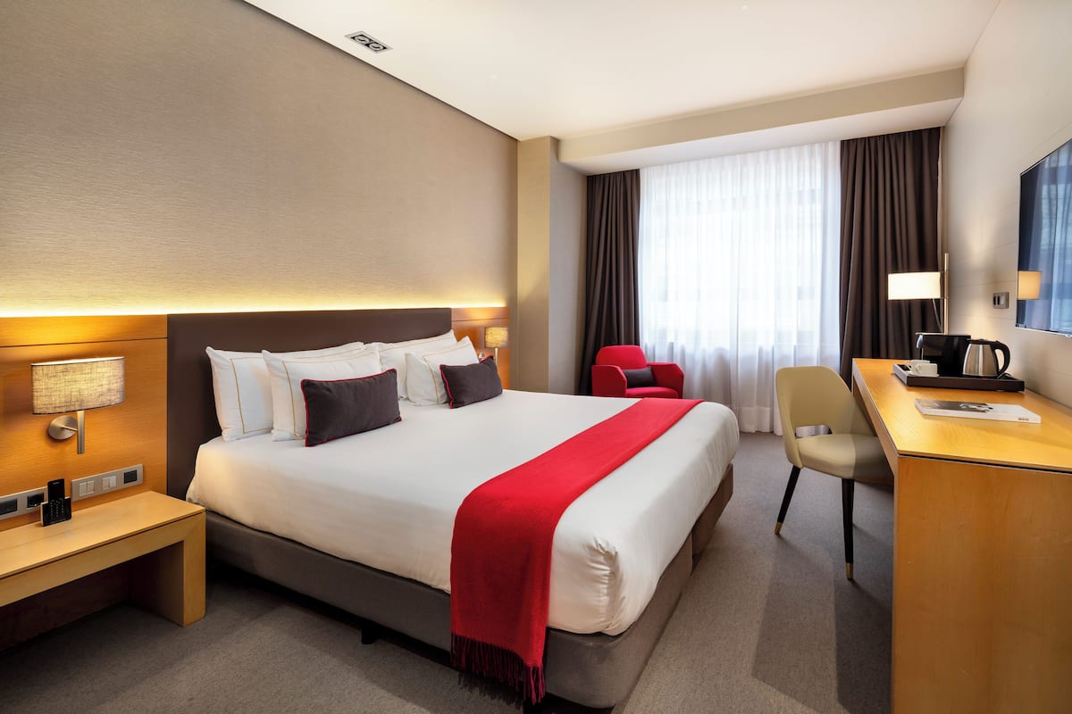 Habitación de hotel con una cama grande, un escritorio, una silla, una lámpara y un televisor.