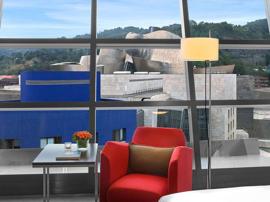 Una habitación de hotel moderna con un ventanal que ofrece vistas a un paisaje urbano y una colina.