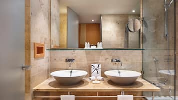 Un baño moderno con dos lavamanos grandes, cabina de ducha con vidrio y tocador de madera.