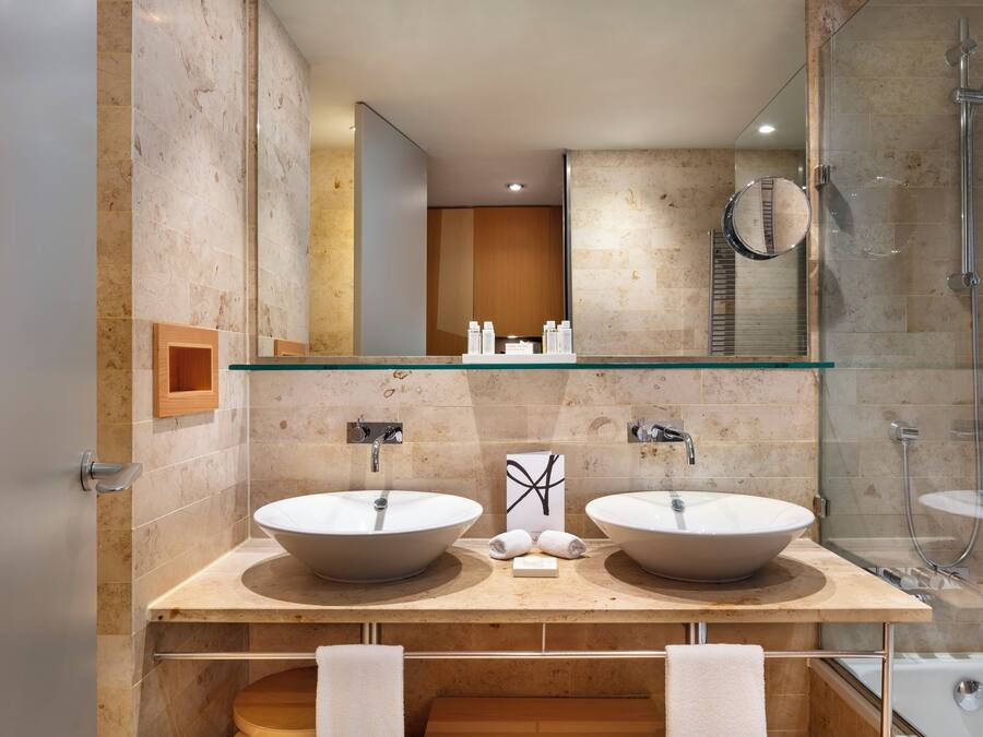 Un baño moderno con dos lavamanos grandes, cabina de ducha con vidrio y tocador de madera.