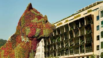 Un bâtiment à l’architecture moderne, doté d’une façade en verre et de plusieurs balcons ornés de verdure.