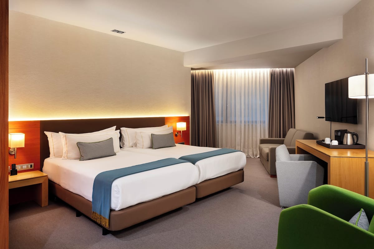 Habitación de hotel con una cama grande, un escritorio, una silla, un televisor y una ventana con cortinas.