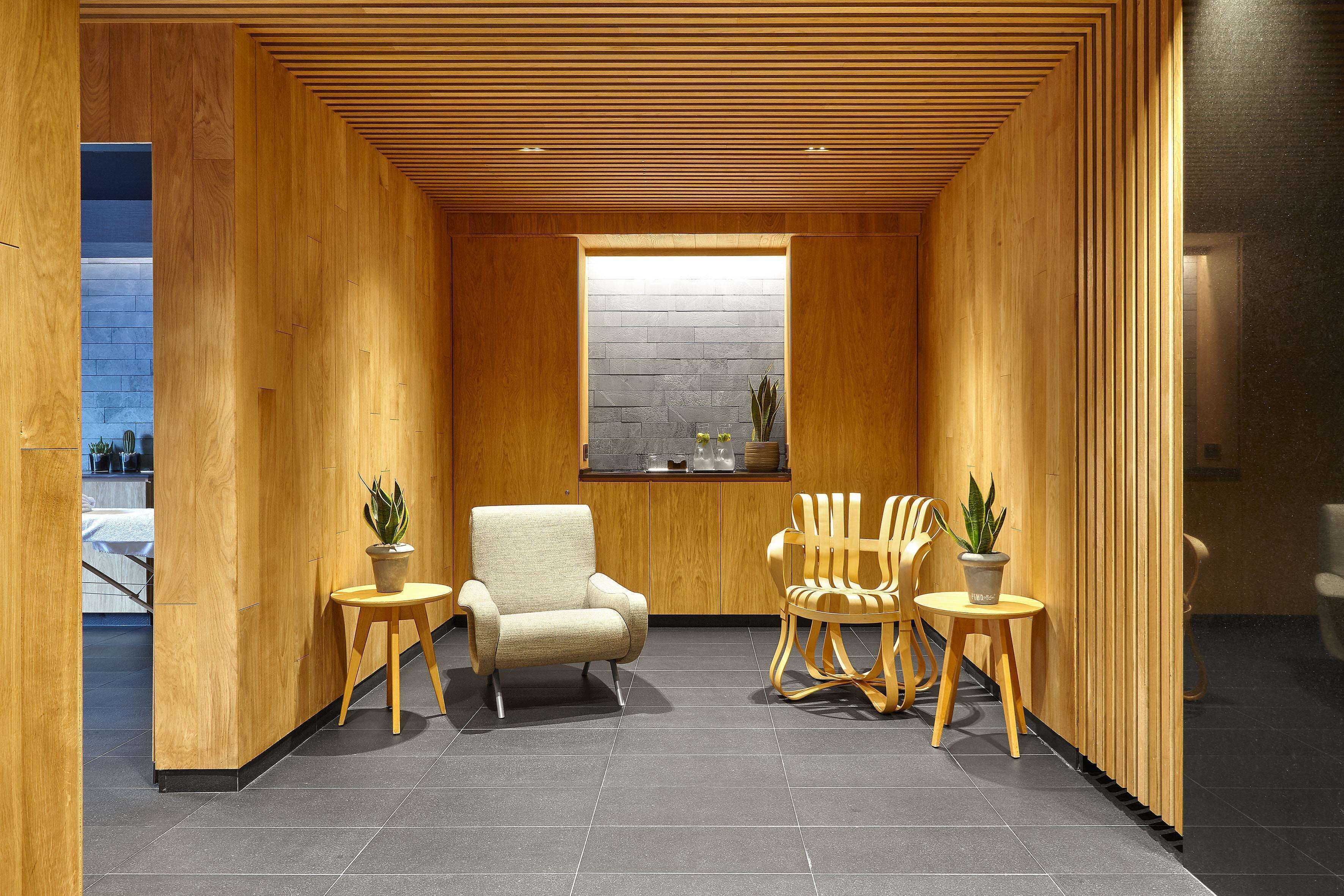 A modern interior with wooden panel walls, a central seating area with two chairs and a sofa, and a small table with a plant.