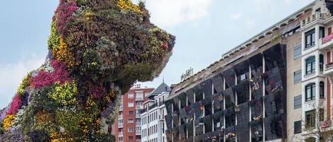 A large floral sculpture resembling a lion's head in an urban plaza with modern buildings in the background.