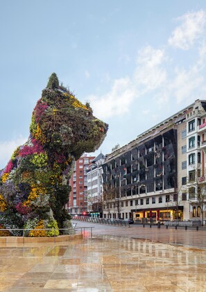 Stunning public square with a majestic lion's head sculpture surrounded by vibrant flowers and a modern building in the background.