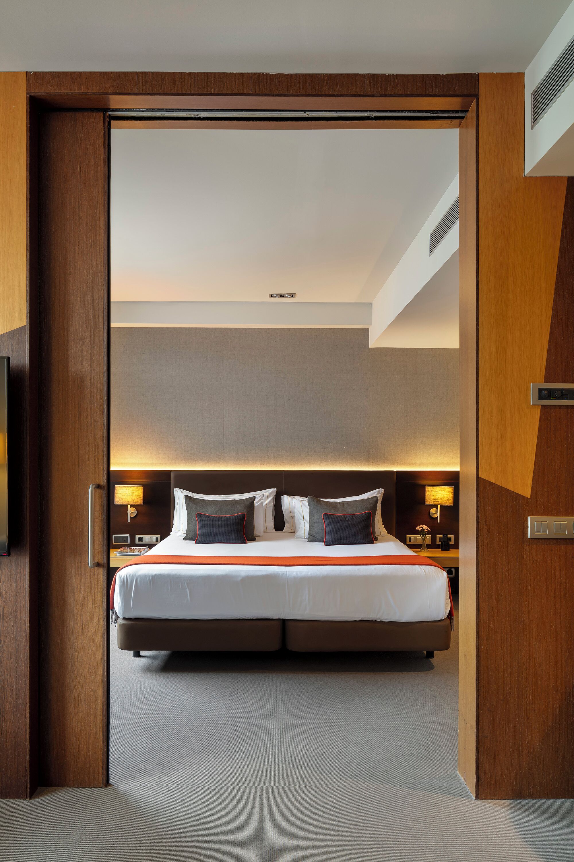 Habitación de hotel con una cama grande, un marco de puerta de madera y una rejilla en el techo.
