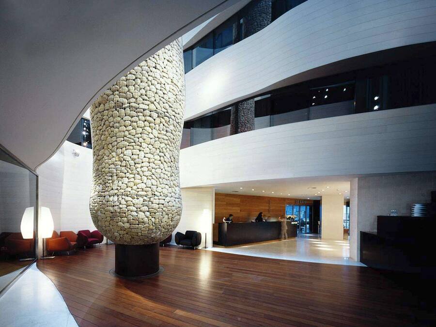 A modern lobby with a unique stone sculpture, wooden flooring, and a reception desk.