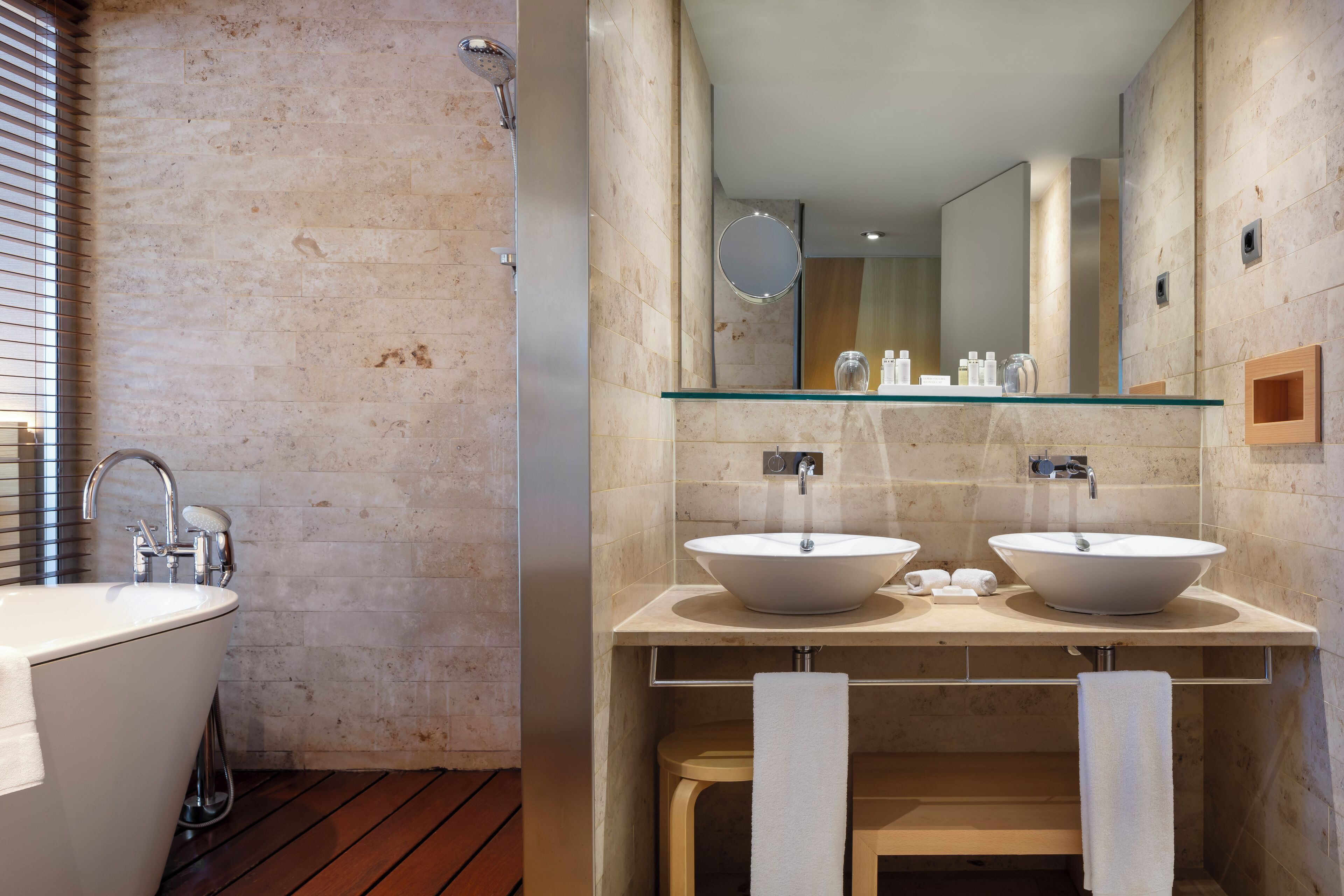 A modern bathroom with a freestanding bathtub, two vessel sinks, a glass shelf, and a large mirror.