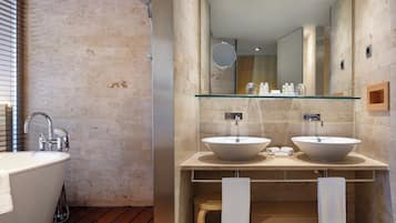 A modern bathroom with a freestanding bathtub, two vessel sinks, a glass shelf, and a large mirror.