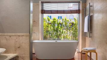 A modern bathroom with a freestanding bathtub, a wooden floor, a window with a view of greenery, and a towel rack.