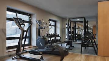 Un gimnasio moderno con máquinas de cardio, equipo de levantamiento de pesas y amplias ventanas con vistas al exterior.