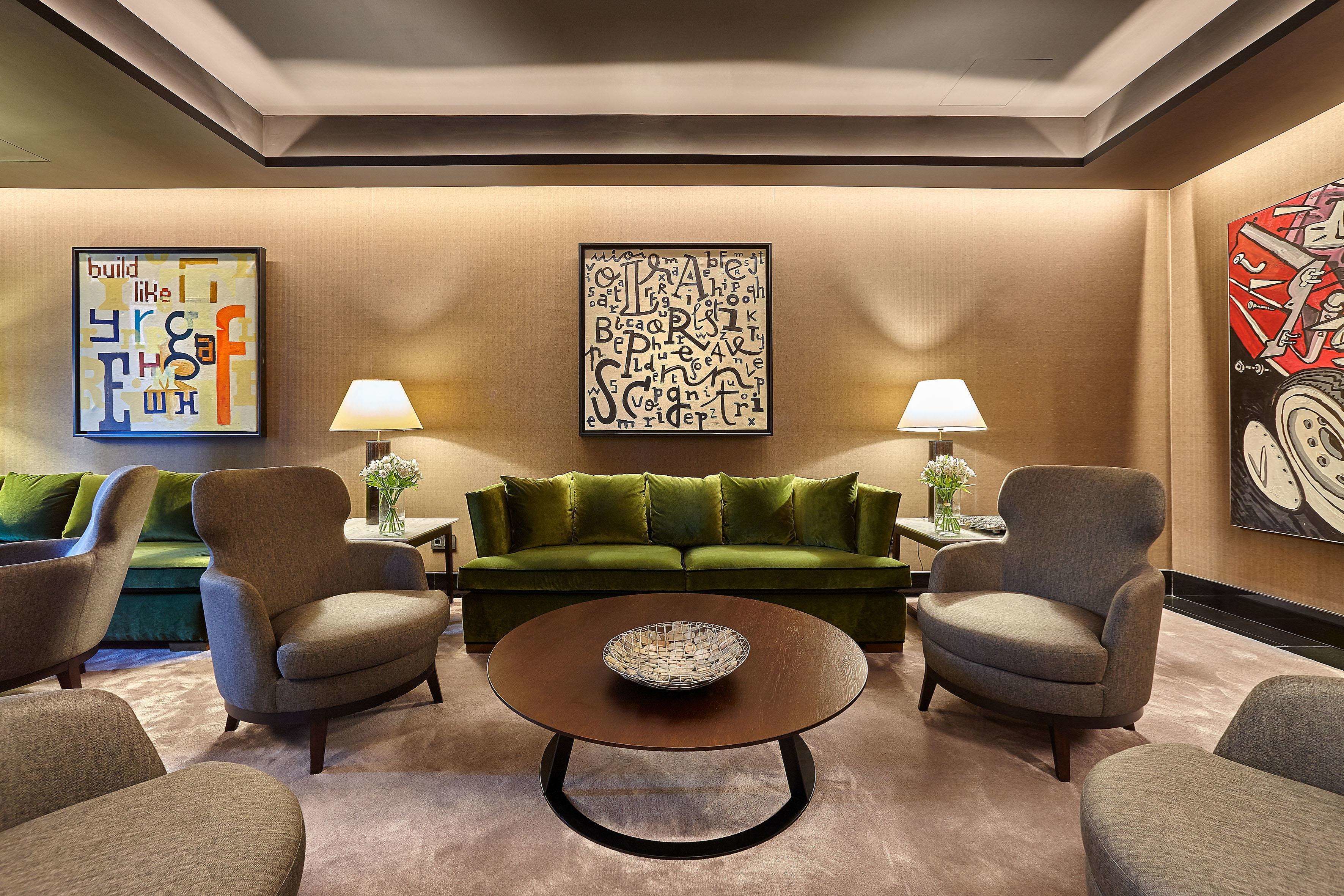 Una sala de estar moderna con un sofá verde, dos sillones, una mesa de centro y dos lámparas.