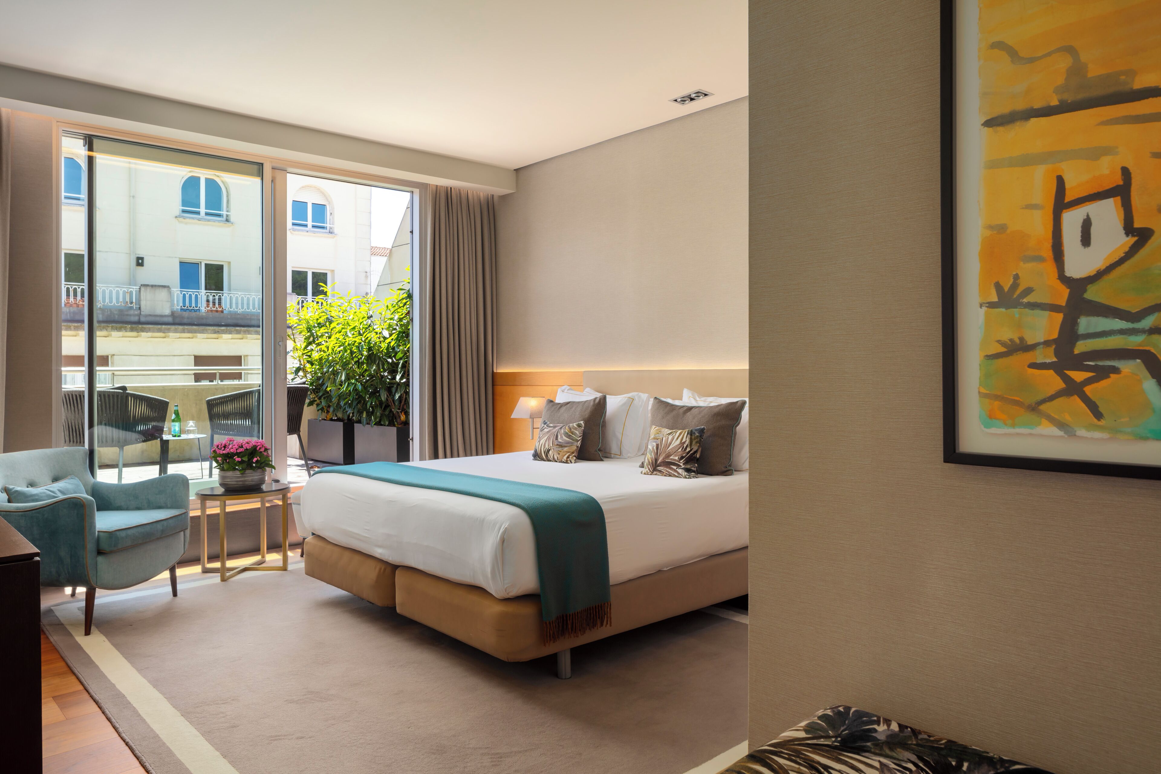 Habitación de hotel con cama, una silla, una mesita, una planta y ventana con vista a edificios.