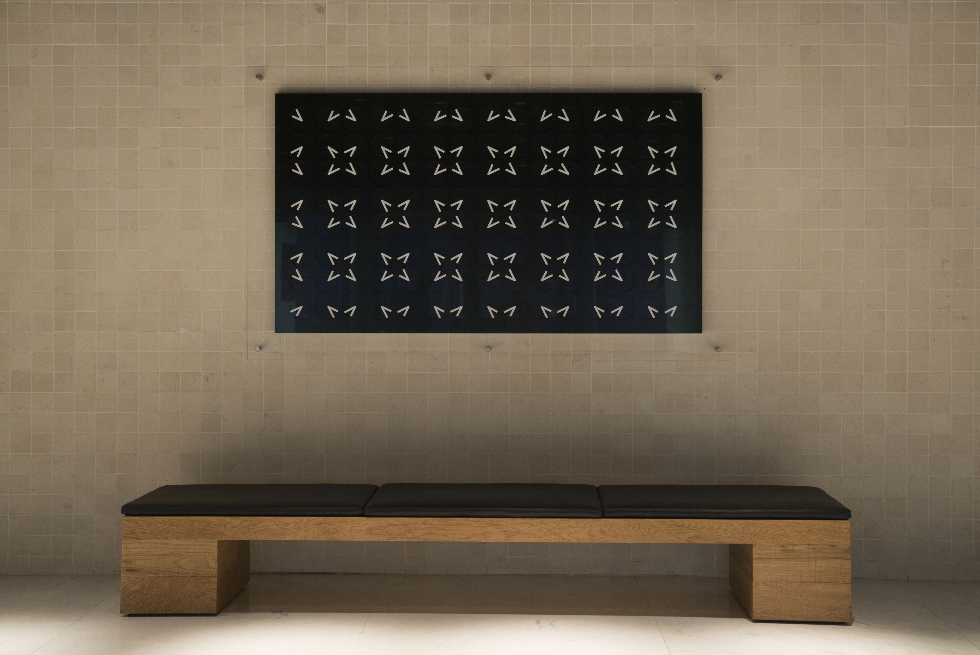 A bench with a dark cushion in front of a wall with a patterned design.