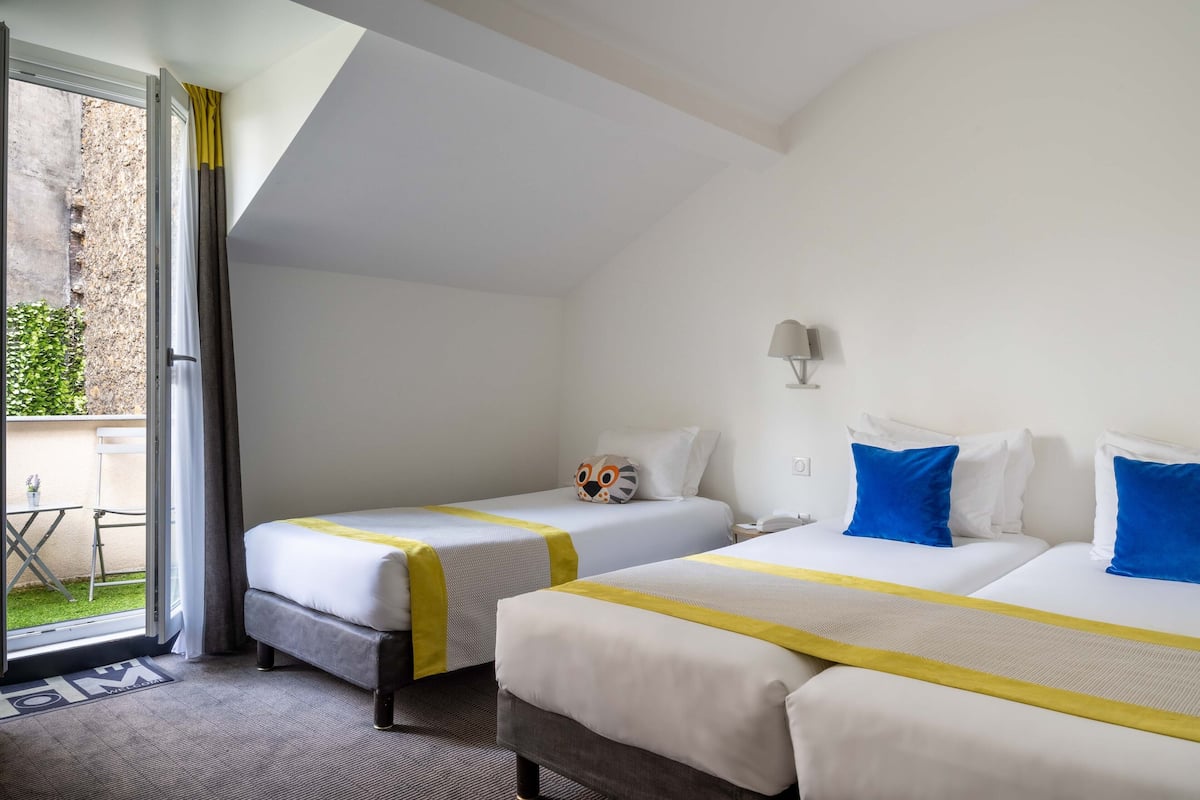 Una habitación de hotel con dos camas, una mesita y vistas a un patio.