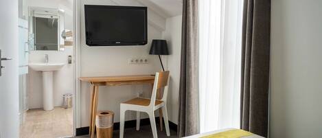 A hotel room with a bed, a desk, a chair, a television, a mirror, a sink, and a window with curtains.