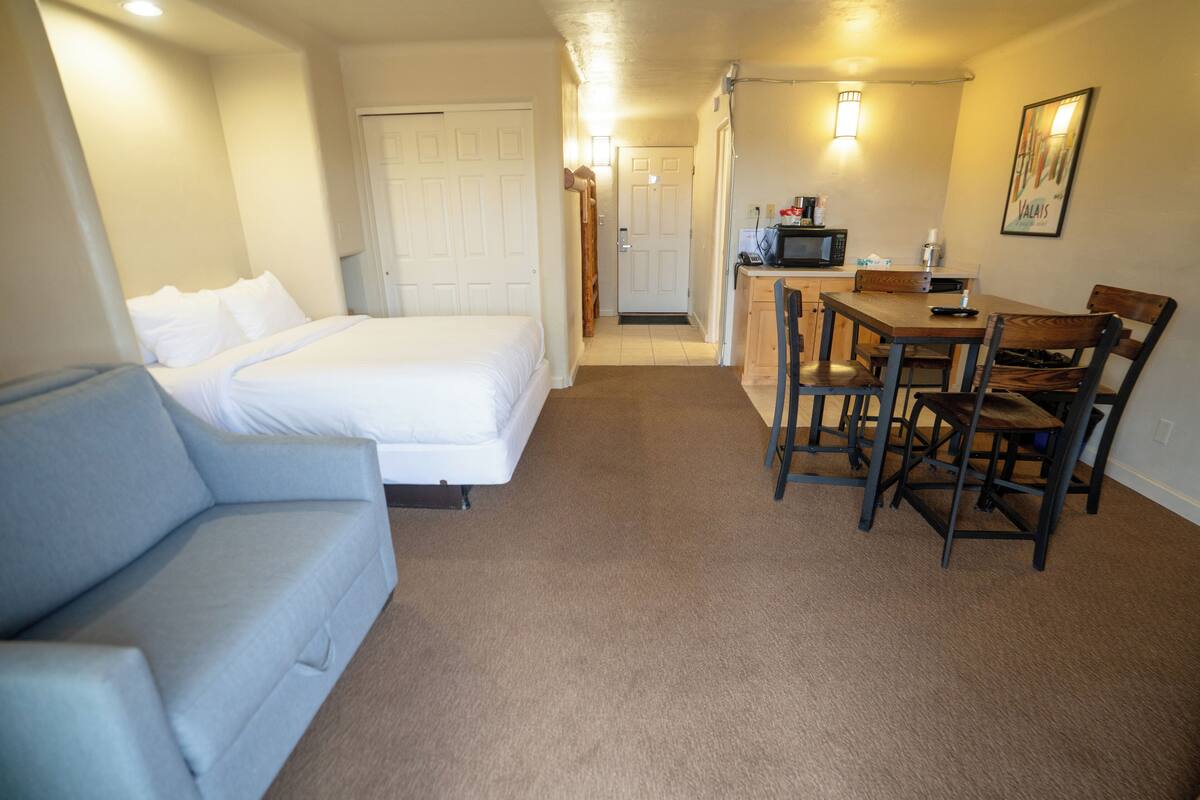 Habitación de hotel con cama, sofá, mesa de comedor con sillas, microondas y una pequeña kitchenette.
