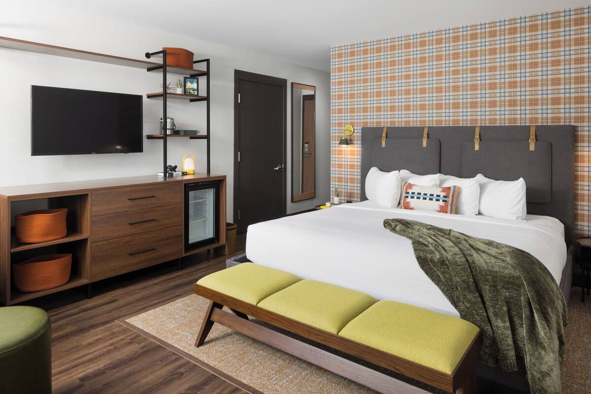 Una habitación de hotel moderna con una cama grande, un televisor de pantalla plana, un aparador de madera y un papel tapiz estampado de cuadros.
