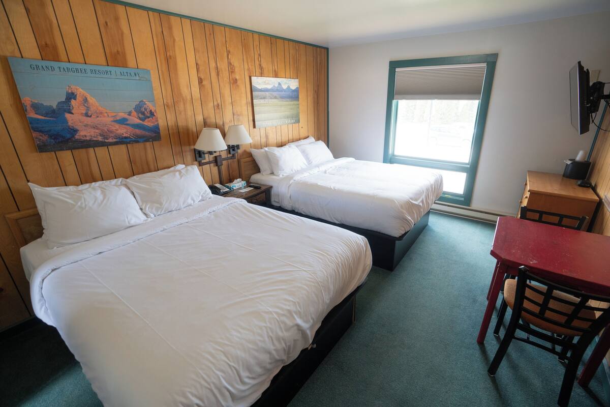 Habitación de hotel con dos camas, un escritorio con silla, una ventana con persianas y lámparas fijadas a la pared.