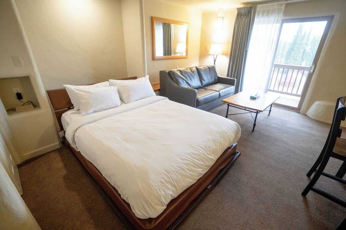 Una habitación de hotel con una cama grande, un sofá, una mesita, un espejo y una ventana con cortinas.