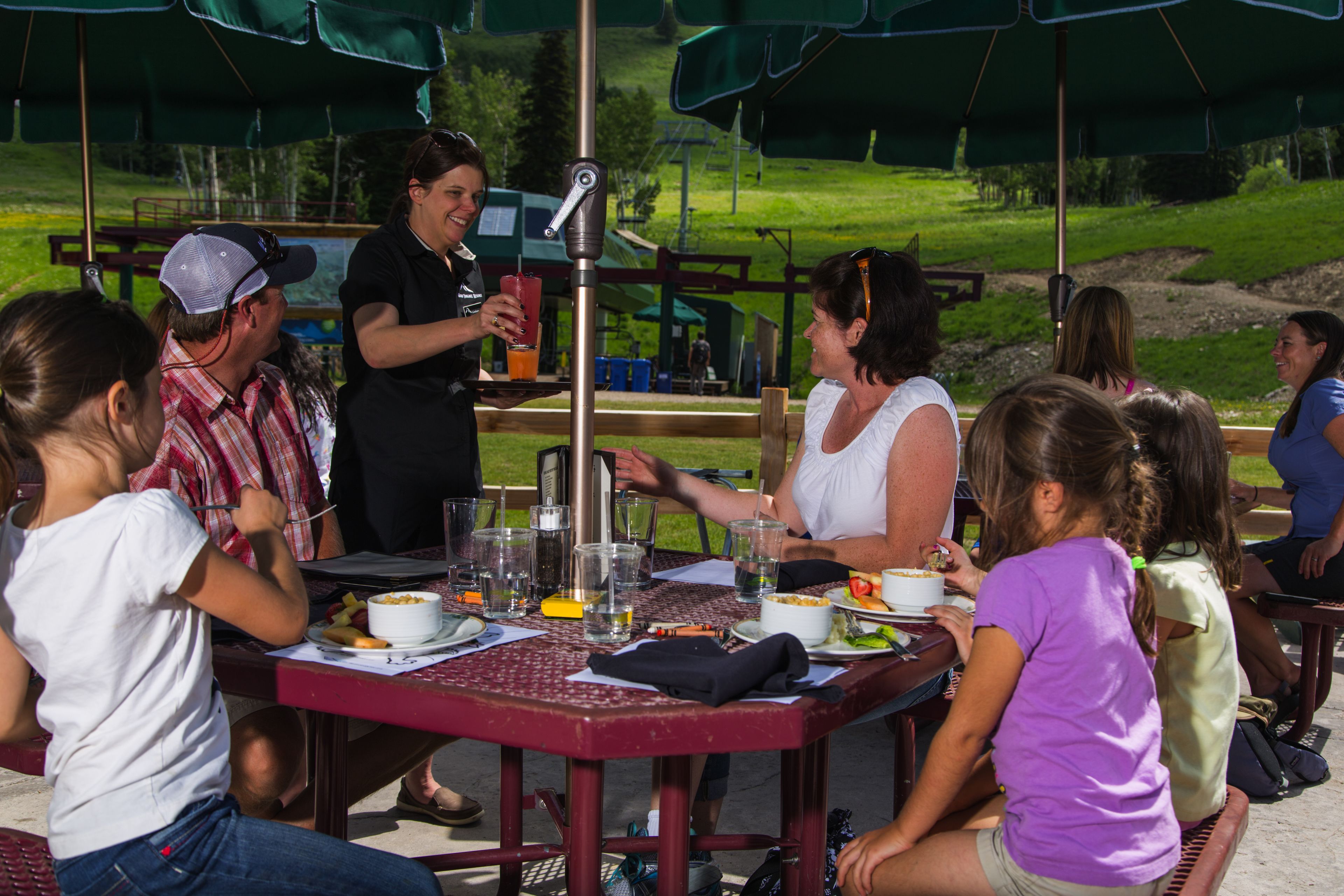 A group of people dining at an outdoor table with a metal frame and green canopy overhead.