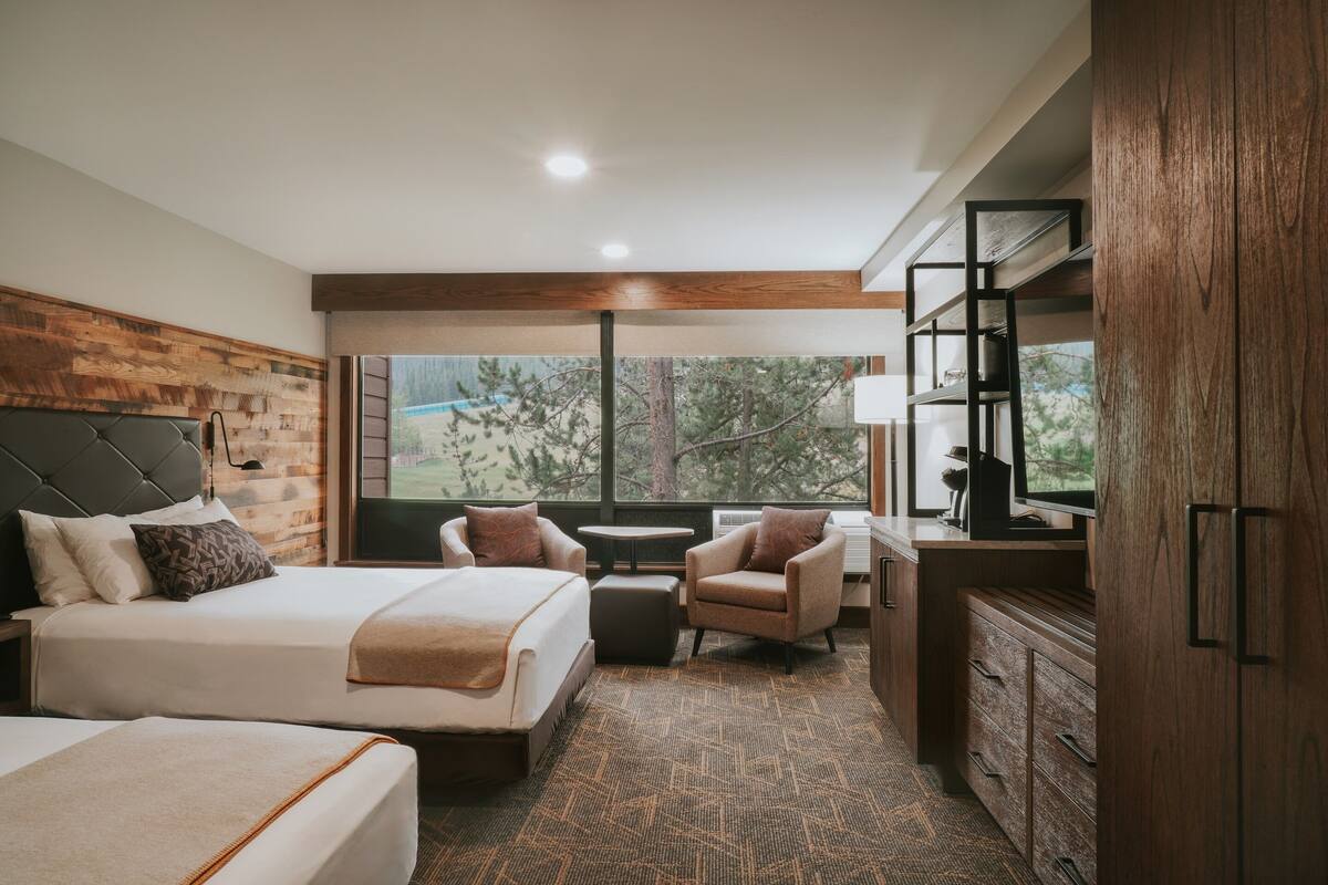 A hotel room with a large bed, two armchairs, a small table, and a TV.