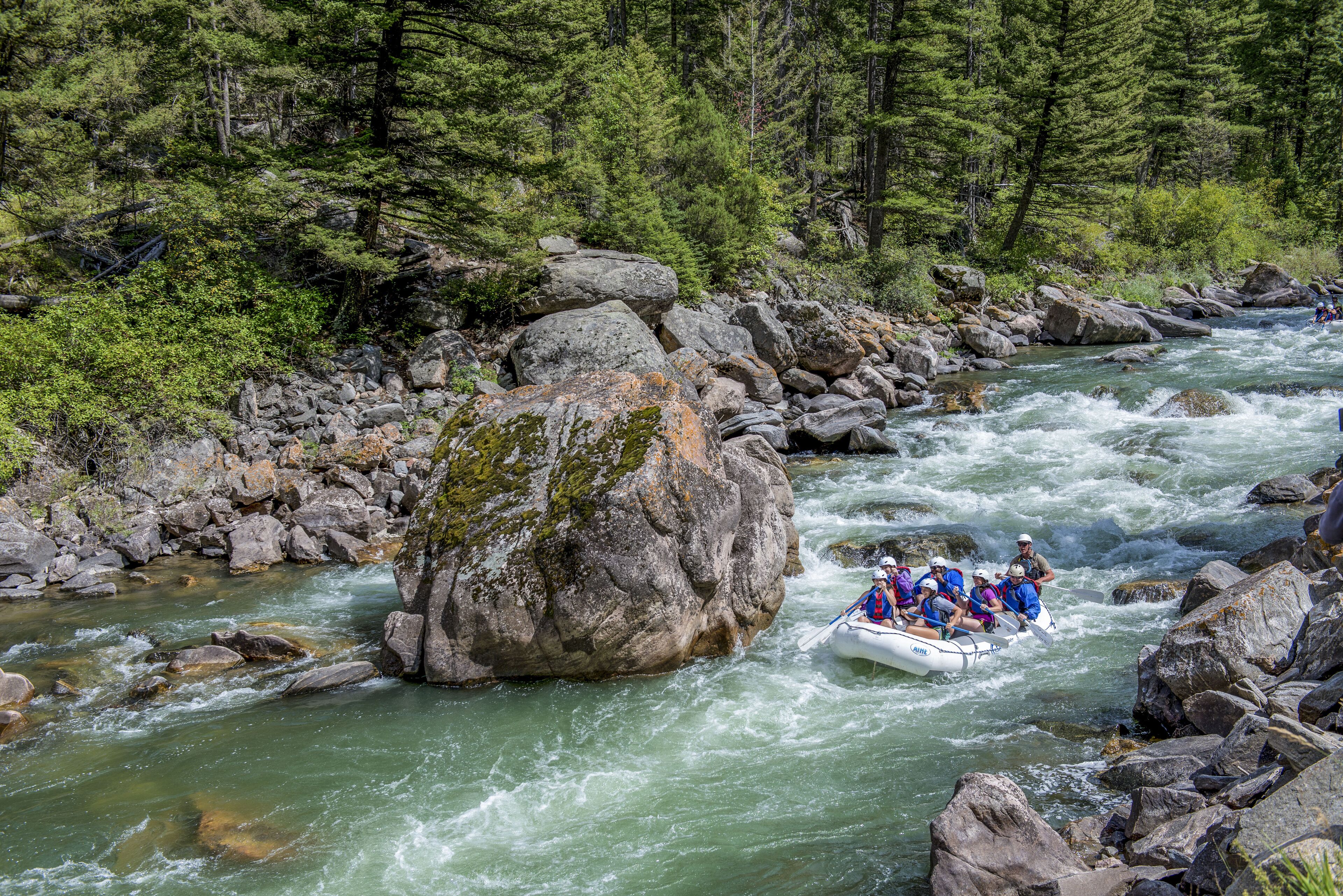 Un río con una balsa navegando por rápidos, rodeado de grandes rocas y un bosque denso.