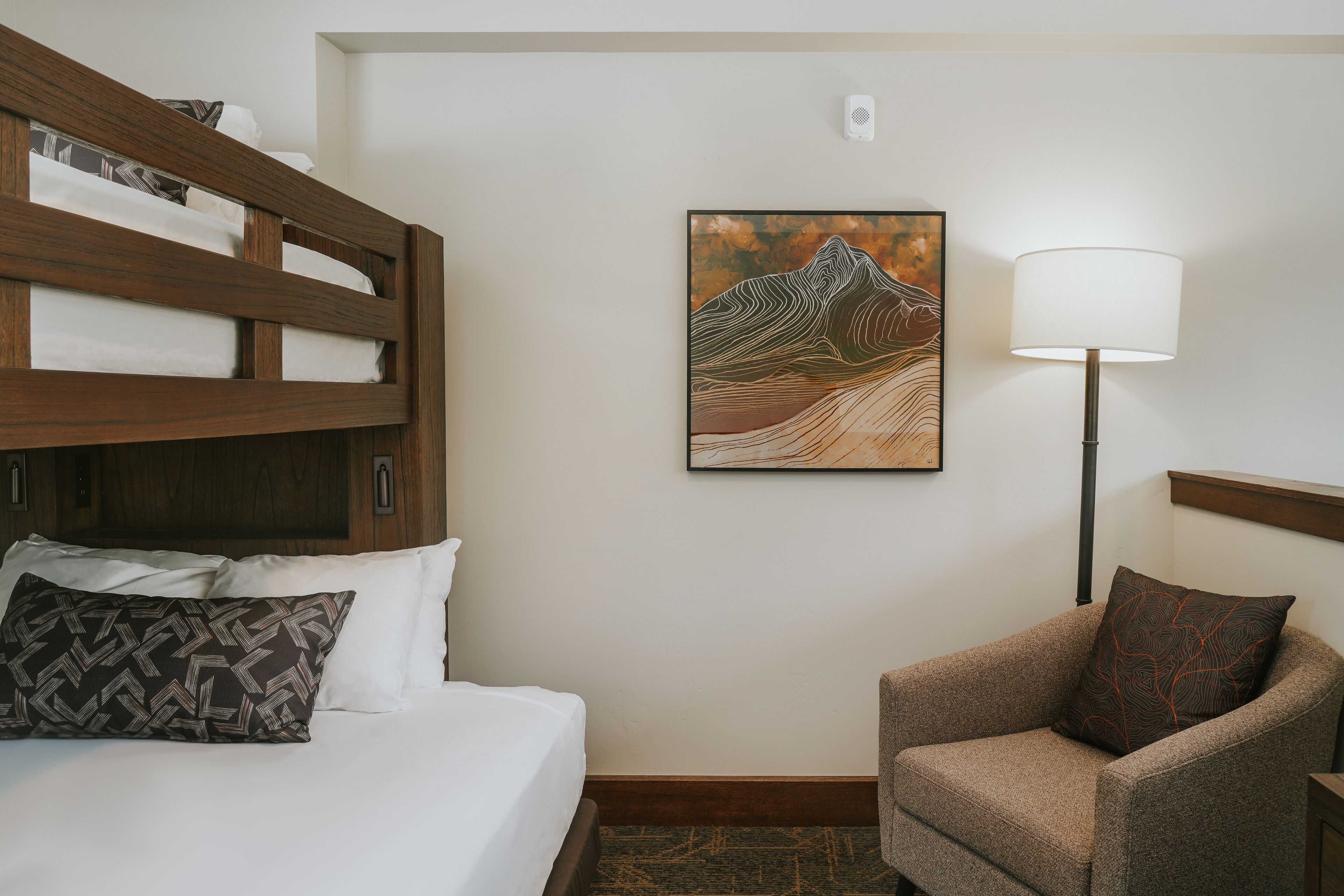 A hotel room with a bed, a chair, a lamp, and a painting on the wall.