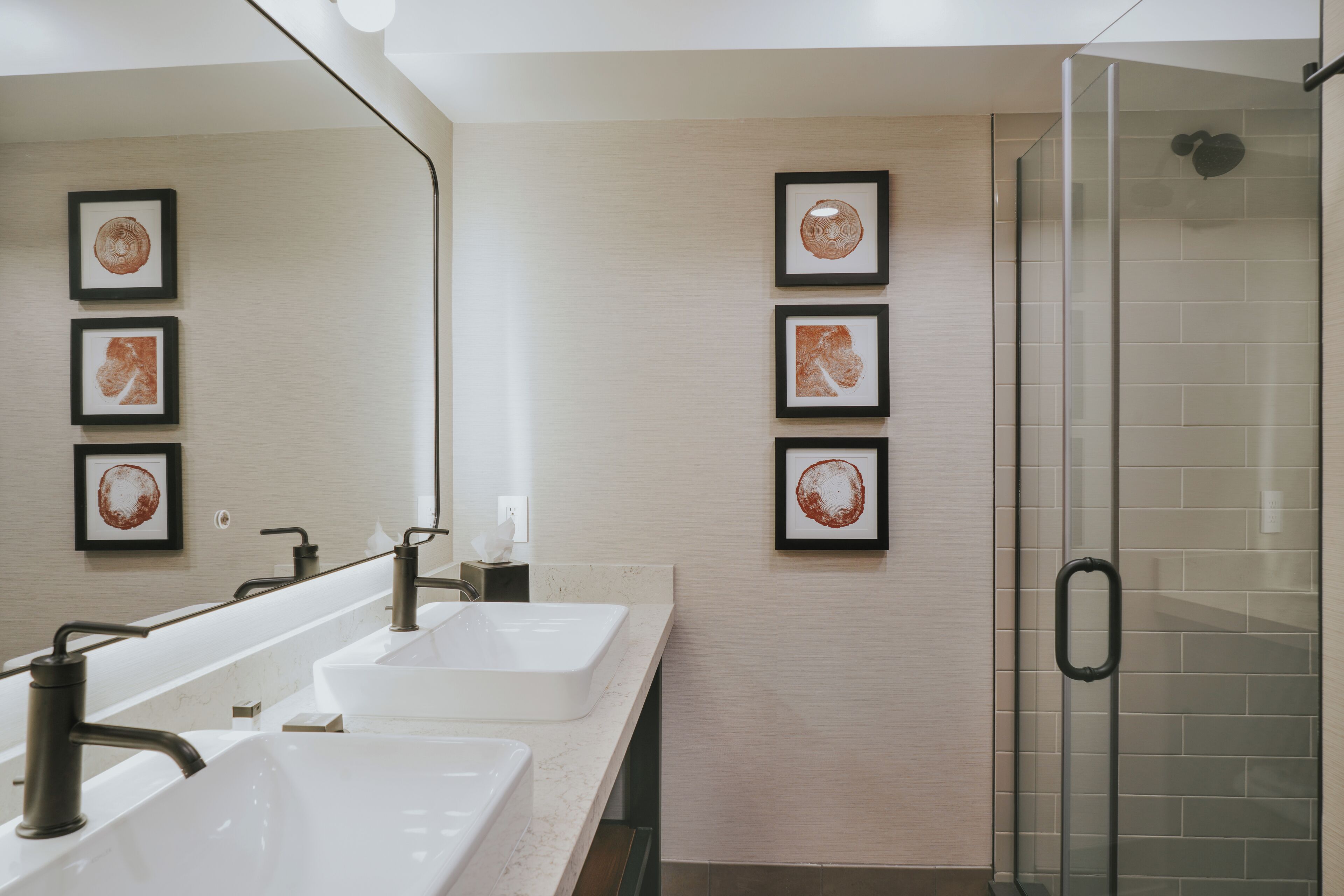 A bathroom with three sinks, a glass shower enclosure, and framed artwork on the wall.