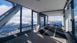 Une pièce aux hauts plafonds, dotée de grandes fenêtres, d’un sol en métal et offrant une vue sur des montagnes enneigées.