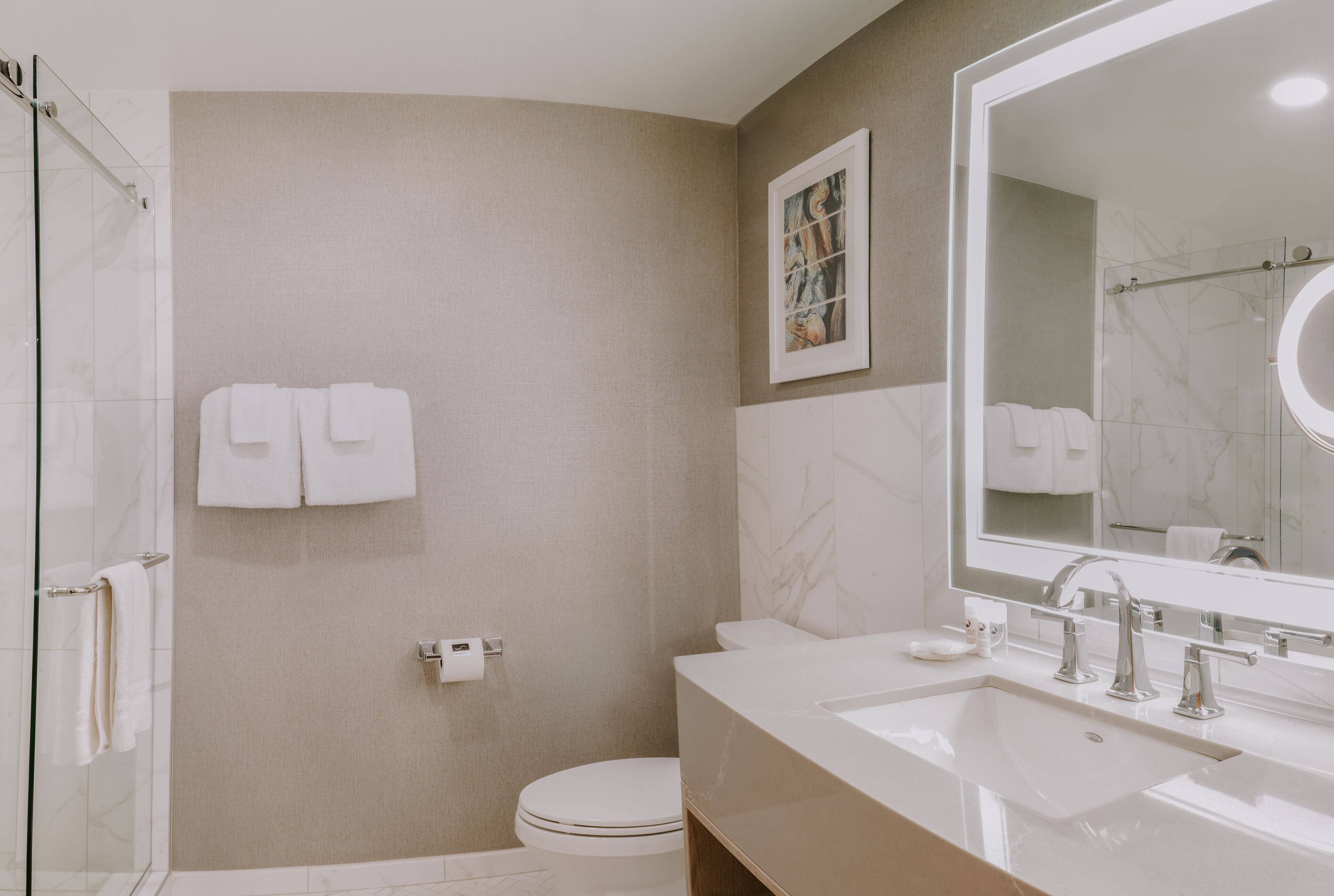 A modern bathroom with a glass shower, a toilet, a sink with a mirror, and towels on the wall.