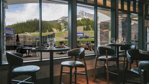 Un restaurant doté de grandes fenêtres offrant une vue sur les montagnes, avec un bar et une vue sur un terrain de golf.