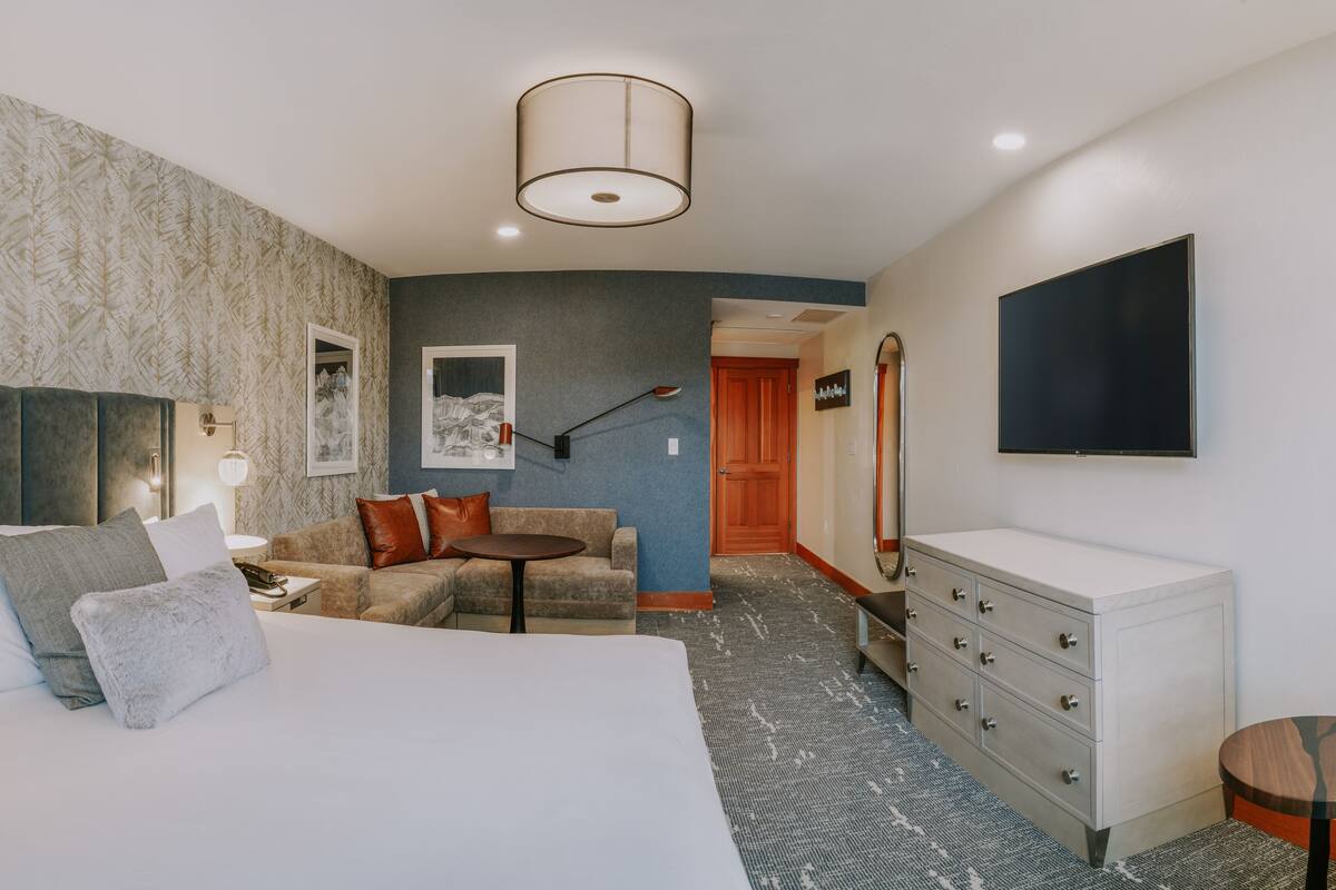 Ein Hotelzimmer mit Bett, einer Couch, einem Schreibtisch, einem Schminktisch, einem Fernseher und einem Flur, der in einen anderen Raum führt.