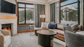 Un salon moderne avec une cheminée, de grandes fenêtres offrant une vue sur les montagnes enneigées, un canapé en cuir et une table basse ronde.
