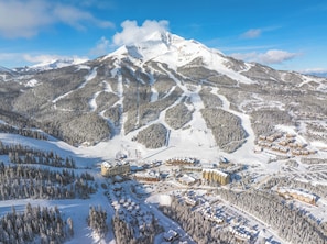 A snow-covered mountain resort with multiple buildings, ski slopes, and dense forested areas.