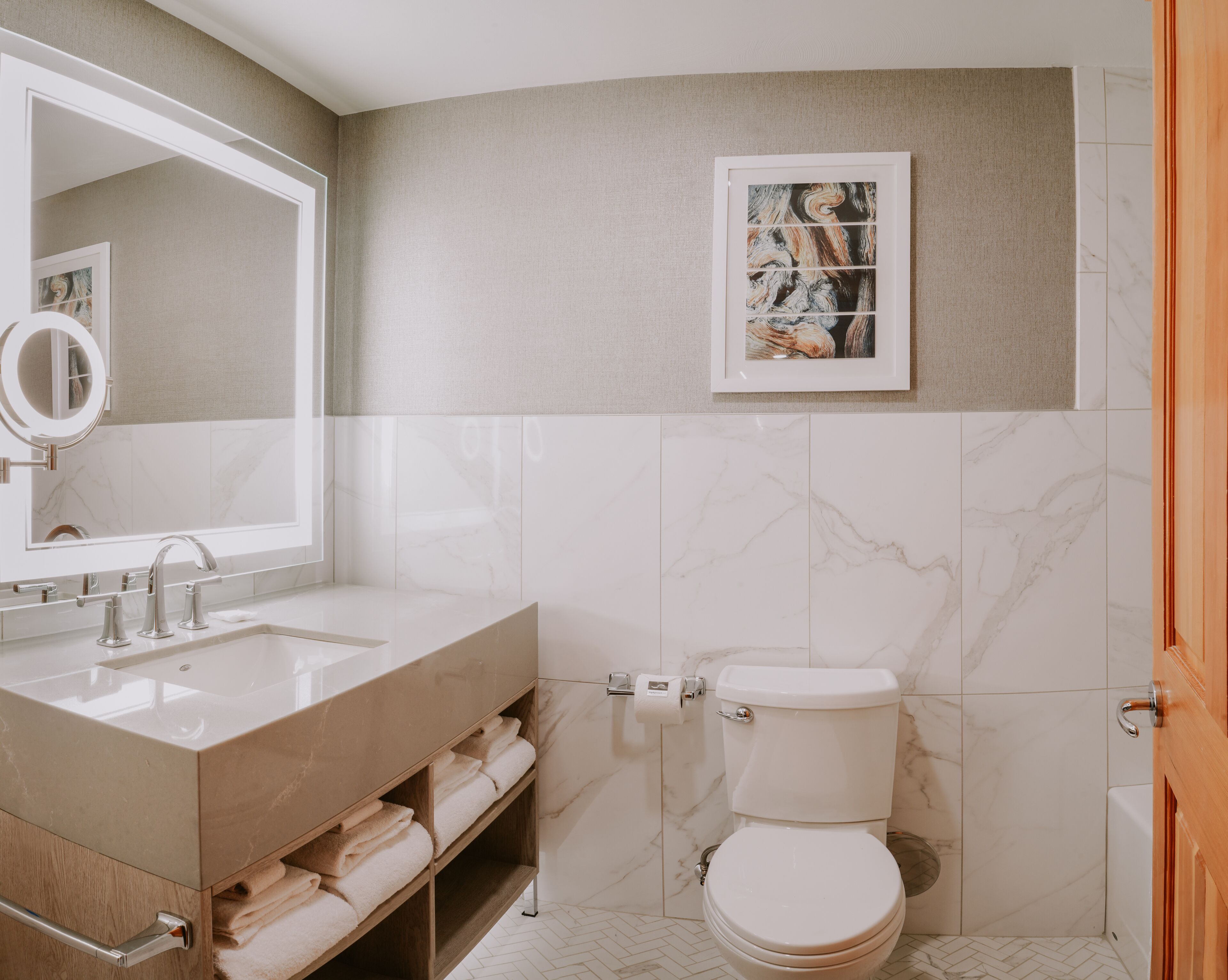 A modern bathroom with a large mirror, a sink, a toilet, and a towel rack.