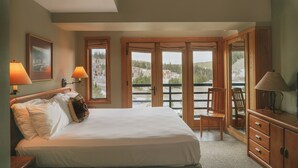 A bedroom with a large bed, two bedside lamps, a wooden dresser, and a view through a glass door to an outdoor area. - Shoshone Condos at Big Sky Resort (Big Sky)