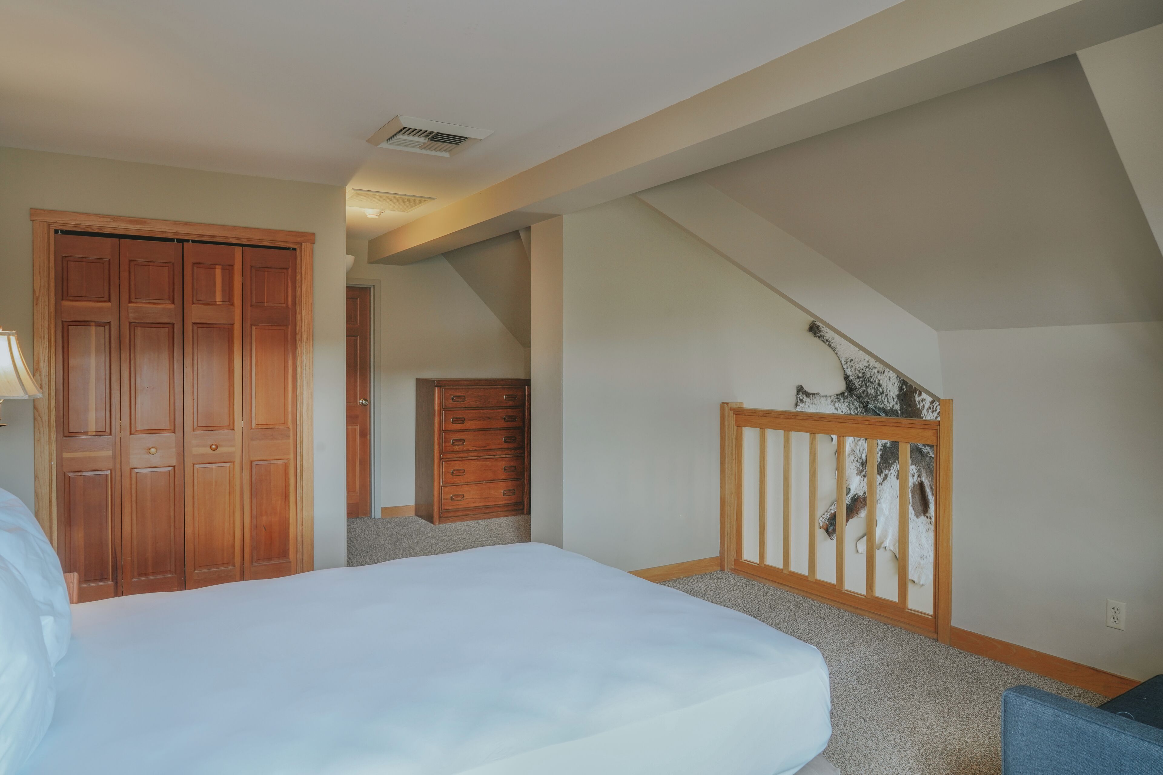 Un dormitorio con cama, armario de madera, cómoda y escalera.