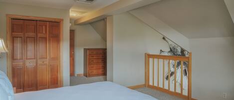 Un dormitorio con cama, armario de madera, cómoda y escalera.