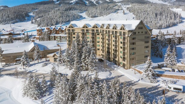 A large hotel with multiple floors and a ski slope in the background. - Shoshone Condos at Big Sky Resort (Big Sky)