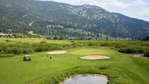 A golf course with bunkers, a pond, and a mountain backdrop. - Shoshone Condos at Big Sky Resort (Big Sky)