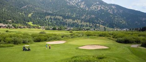 A golf course with bunkers, a pond, and a mountain backdrop.