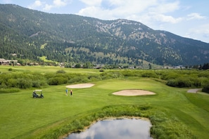 Un parcours de golf agrĂ©mentĂ© de bunkers, dâun Ă©tang et dominĂ© par une chaĂźne de montagnes.