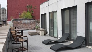 An outdoor patio with lounge chairs and a table, a brick wall, and a modern building facade. - Loft 523 New Orleans (New Orleans)