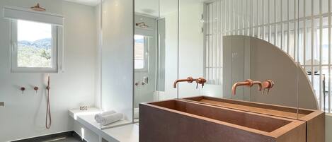 A modern bathroom with a large rectangular sink, a glass shower enclosure, and a bench with a towel.
